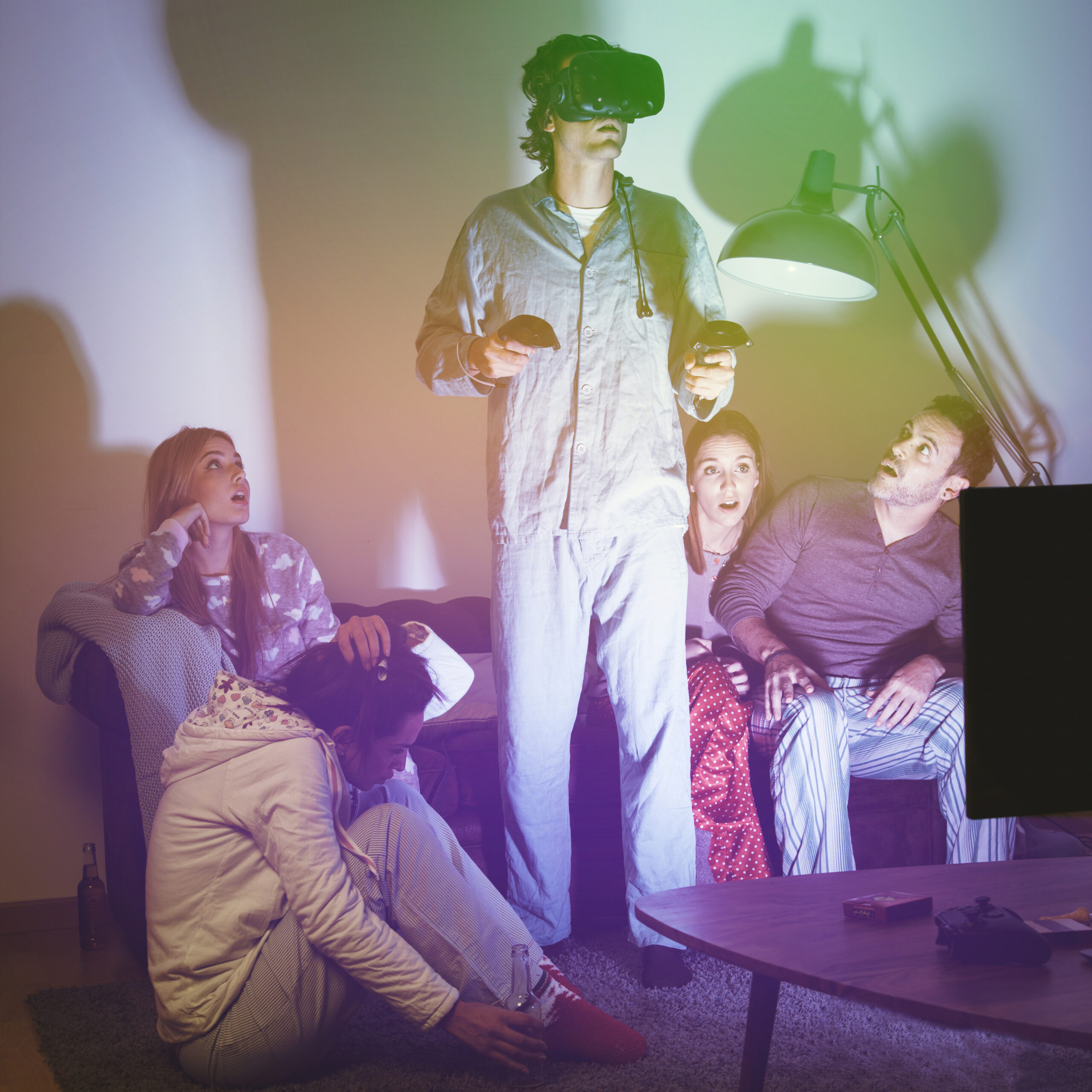 Grupo de personas en casa observando a un hombre con gafas de realidad virtual y mandos en las manos.